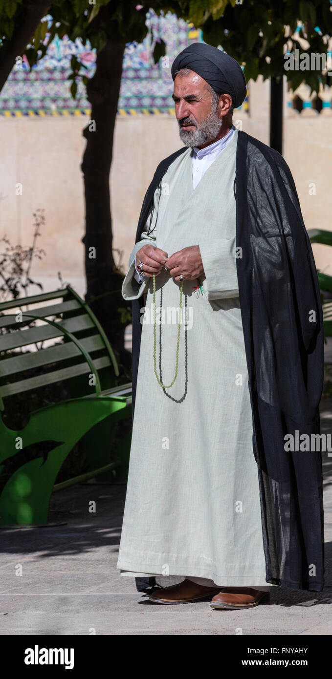 Mullah in turban and robe with worry beads stands in courtyard of Khan Medrassah, Shiraz, Iran Stock Photo