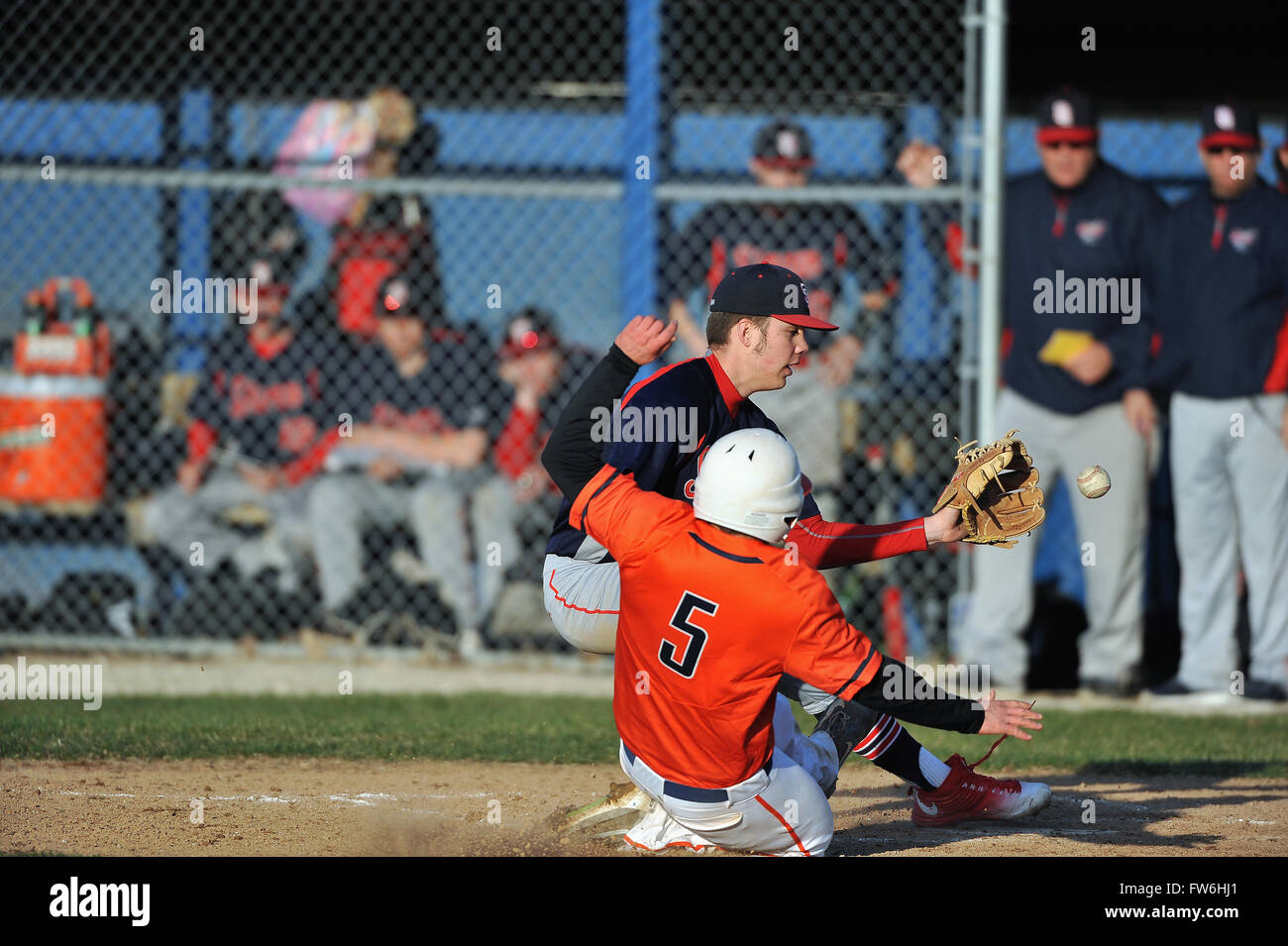 Following a wild pitch, a high school pitcher taking a throw from his catcher while covering the plate as a runner scores. USA. Stock Photo