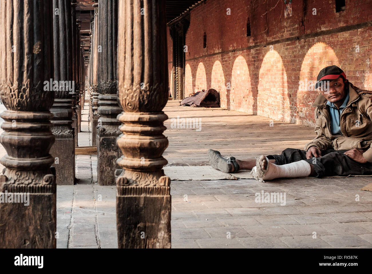 A poor man with a broken leg resting in a public building in Kathmandu Stock Photo