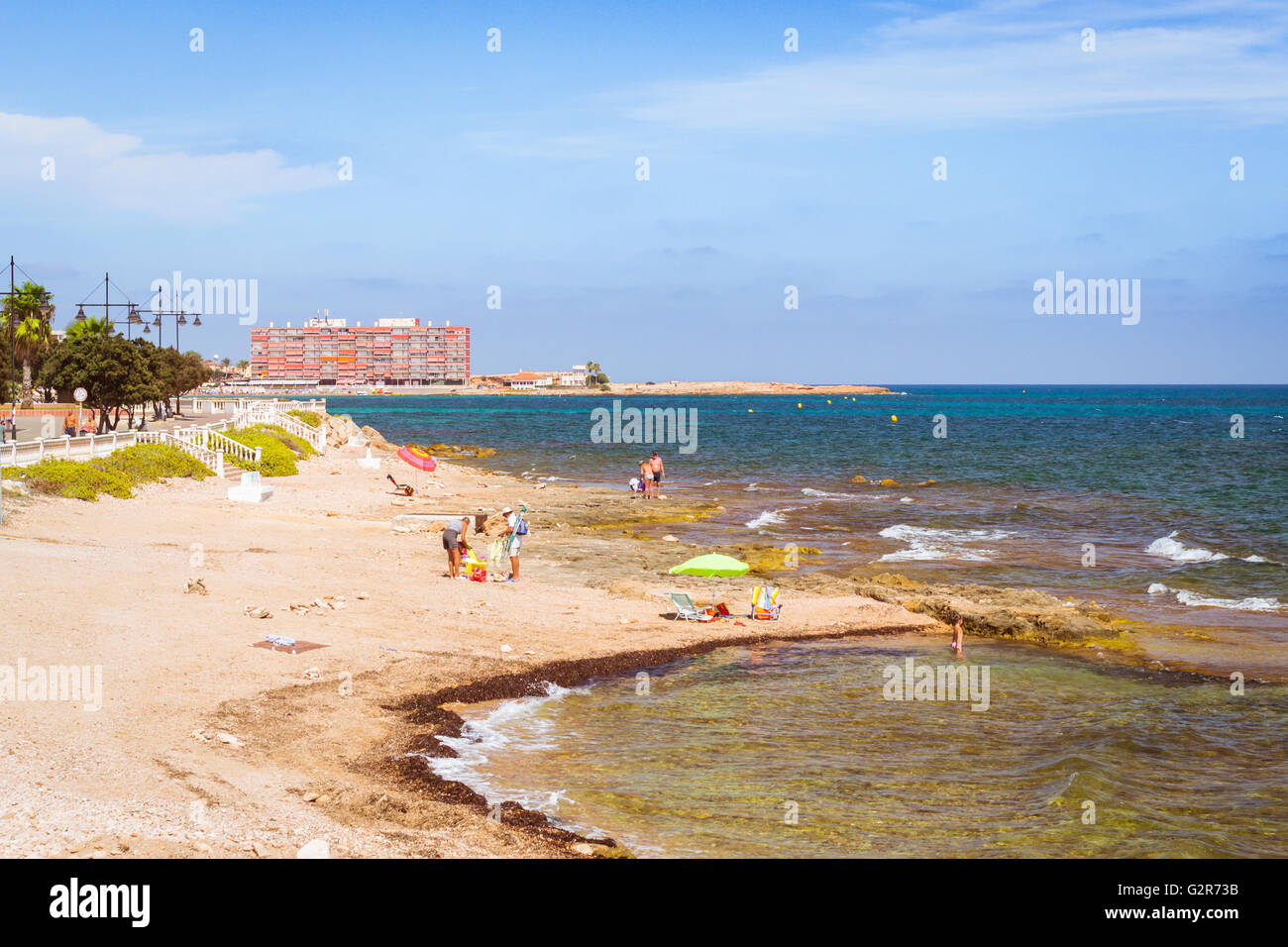 Sunny Mediterranean beach, Tourists relax on warm sand on loungers under parasols. People bathe in salty water, Torrevieja Stock Photo