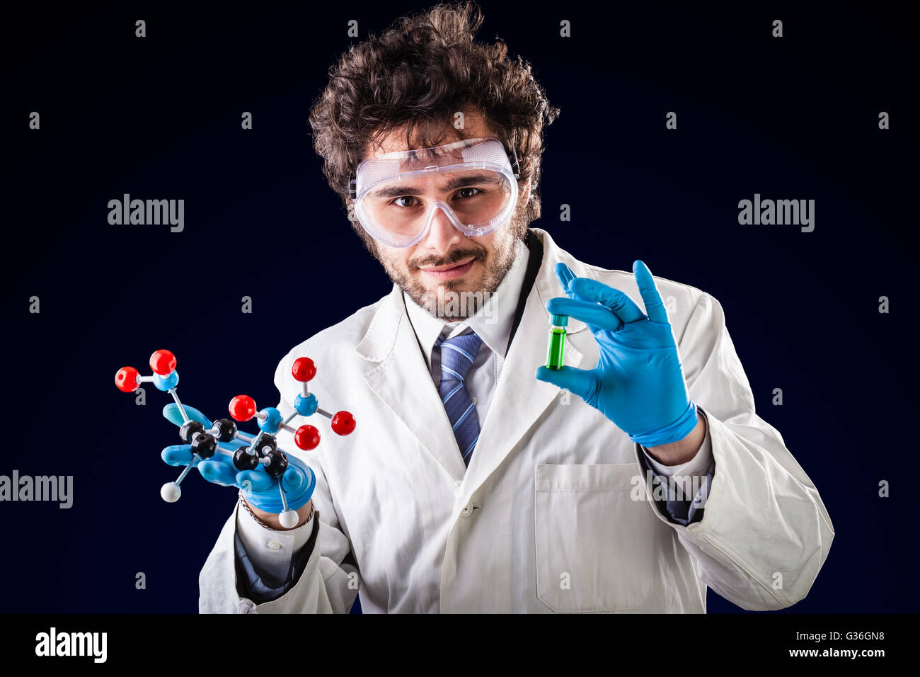 a doctor or researcher with a white lab coat holding a trinitrotoluene tnt molecular model and a vial with green fluid Stock Photo