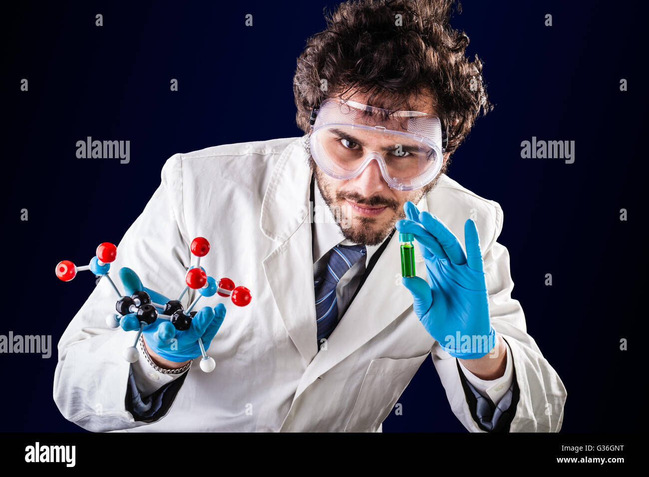 a doctor or researcher with a white lab coat holding a trinitrotoluene tnt molecular model and a vial with green fluid Stock Photo