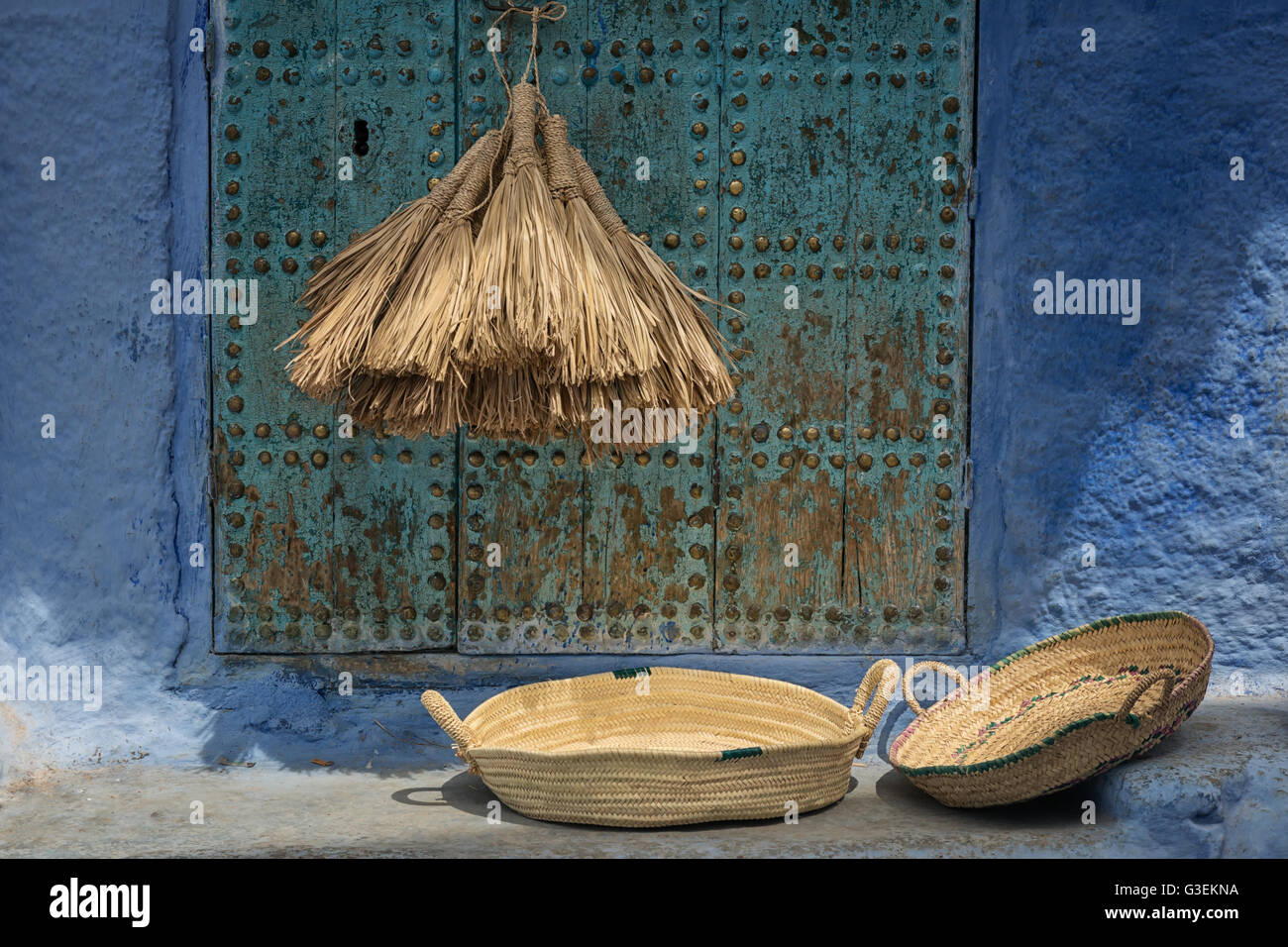 Still life of natural straw brooms and two baskets against old, blue door. Stock Photo