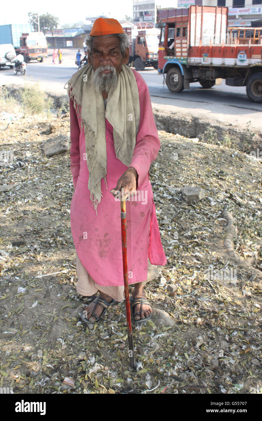 An old poor man from India on the streetside walking with his stick. Stock Photo