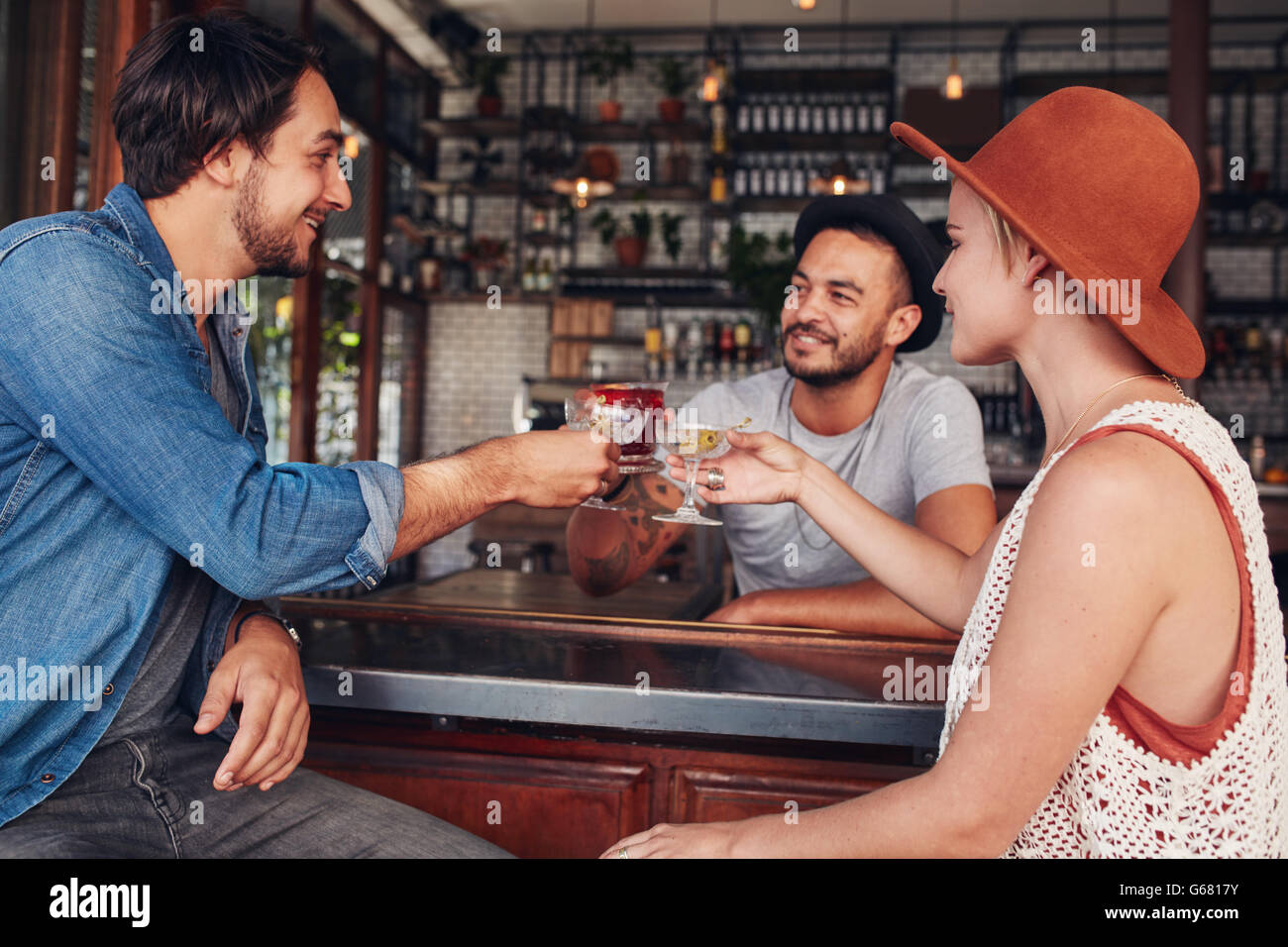 Three young people toasting drinks at cafe. Young men and woman having a glass of drink at bar. Stock Photo