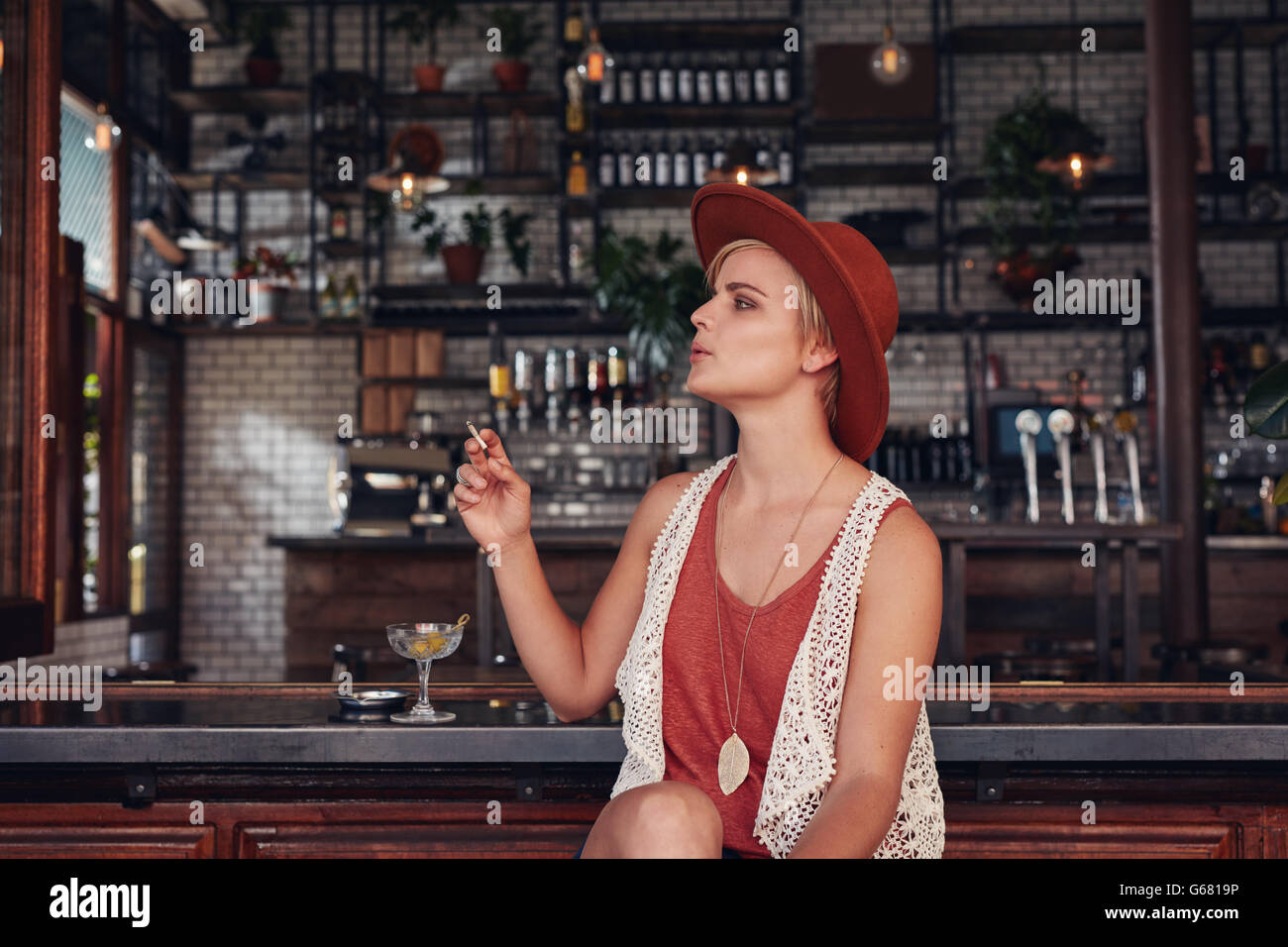 Portrait of attractive young woman smoking in a bar. Holding cigarette and looking away. Stock Photo