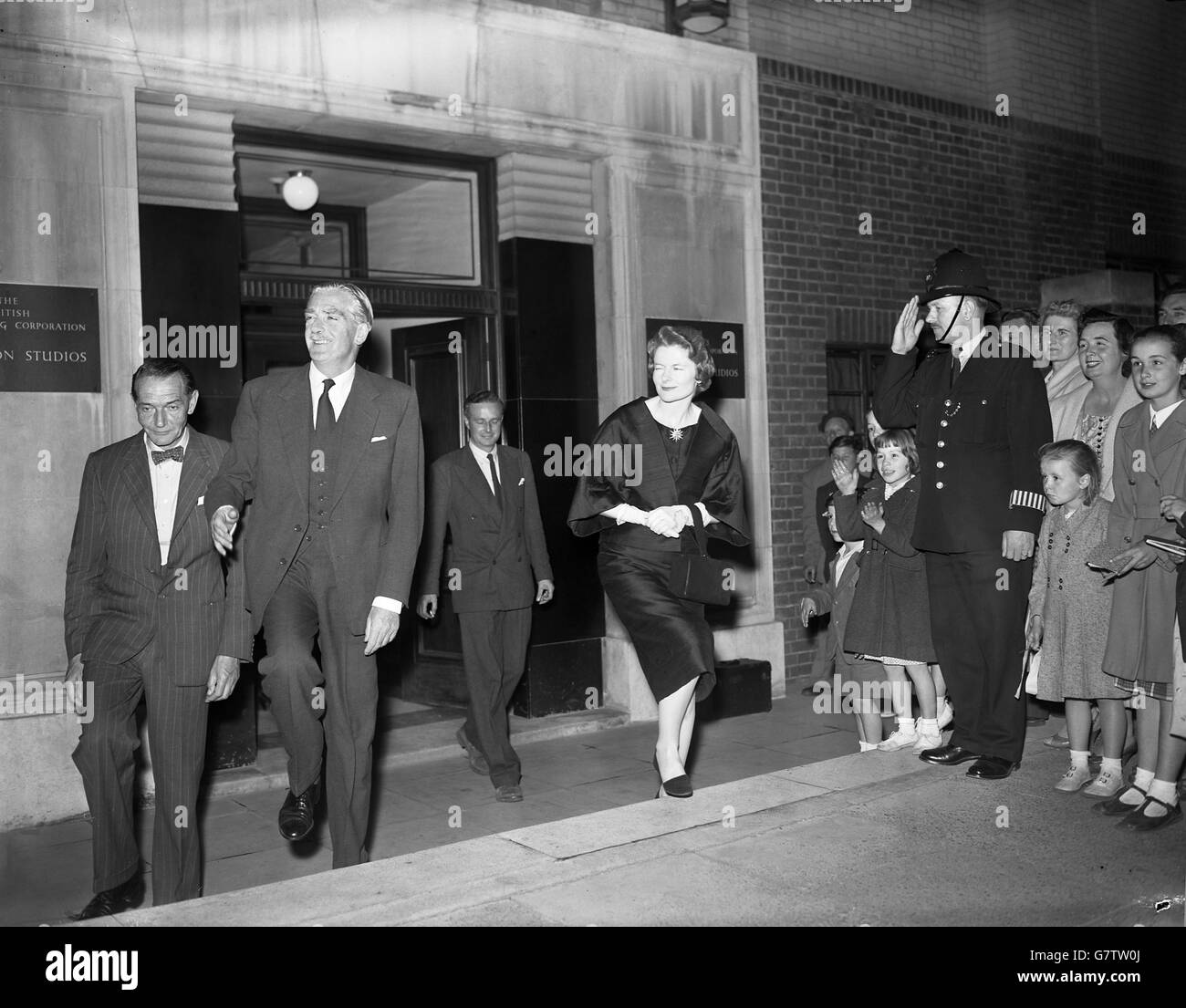 Sir Anthony Eden, Prime Minister, is saluted by a policeman standing in front of a group of bystanders as, accompanied by Lady Eden, he leaves the BBC television studios at Lime Grove, London, after making his 14 minute speech to the nation on the Suez Canal Crisis. The premier was seen by viewers of both BBC and Independent television, and his speech was also broadcast on radio. 'If Colonel Nasser's action were to succeed', he said, 'each one of us would be at the mercy of one man for the supplies upon which we live. We could never accept that'. Stock Photo