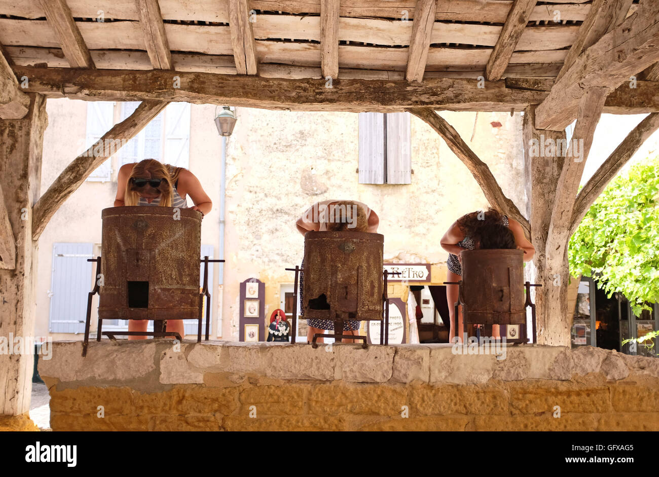 Monpazier market square with tin weighing buckets in Dordogne Region with women looking inside barrels Stock Photo