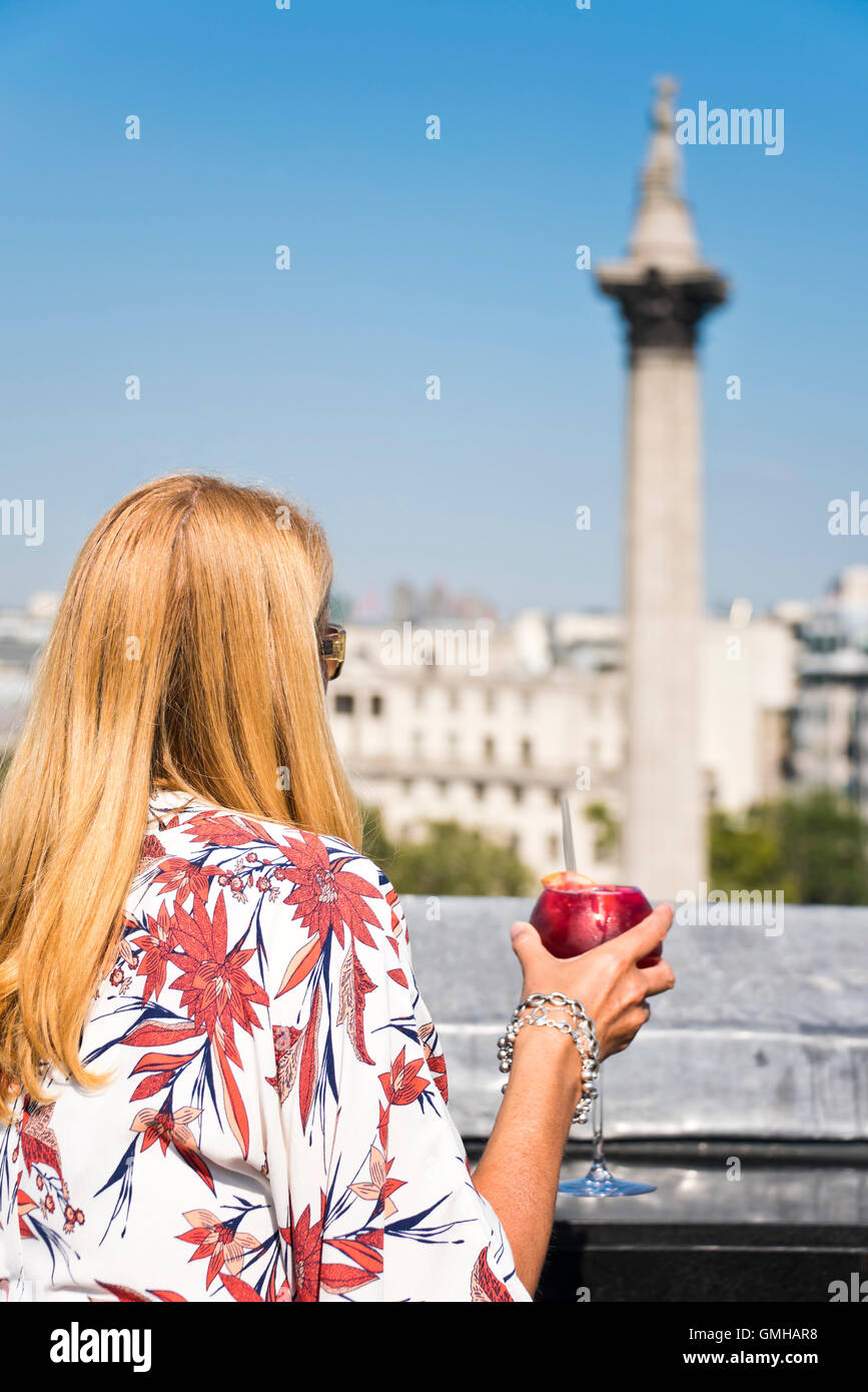 Vertical portrait of a woman enjoying a cocktail overlooking Nelson's Column in Trafalgar Square, London, in the sunshine. Stock Photo