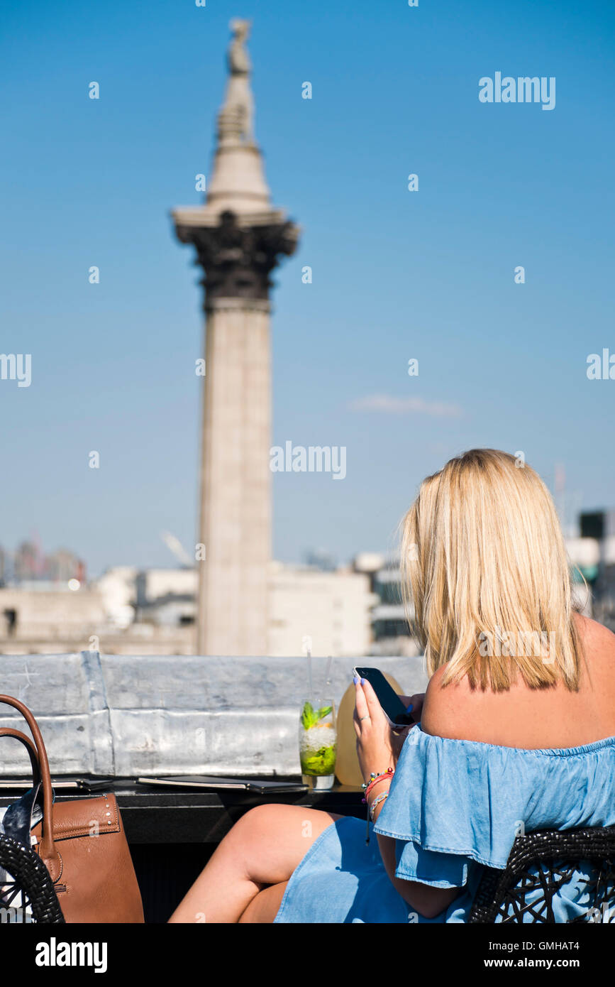 Vertical portrait of a woman enjoying a cocktail overlooking Nelson's Column in Trafalgar Square, London, in the sunshine. Stock Photo