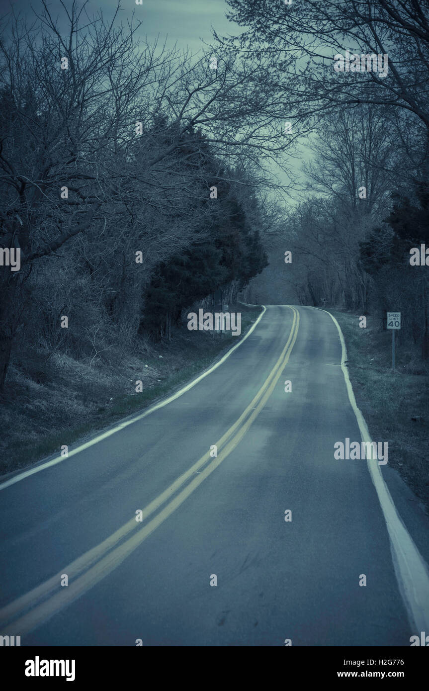 A dark eery creepy two lane road in the middle of nowhere, deep within the dark woods of Virginia. Stock Photo