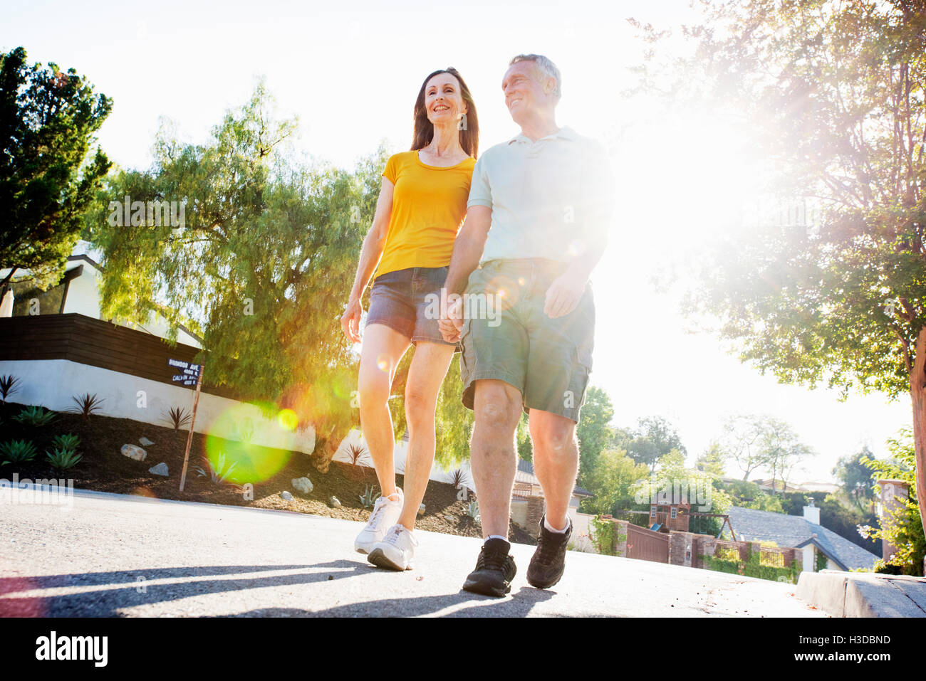 Senior couple wearing shorts walking along a street in the sunshine. Stock Photo