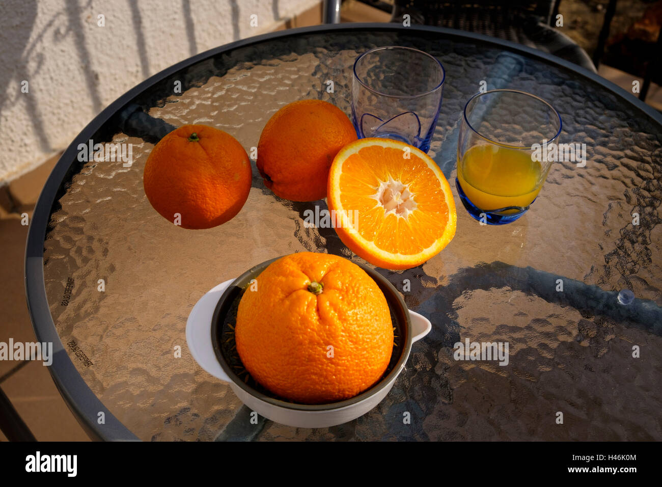 Orange juicer, glasses  and cut orange on a glass table outside without people Stock Photo