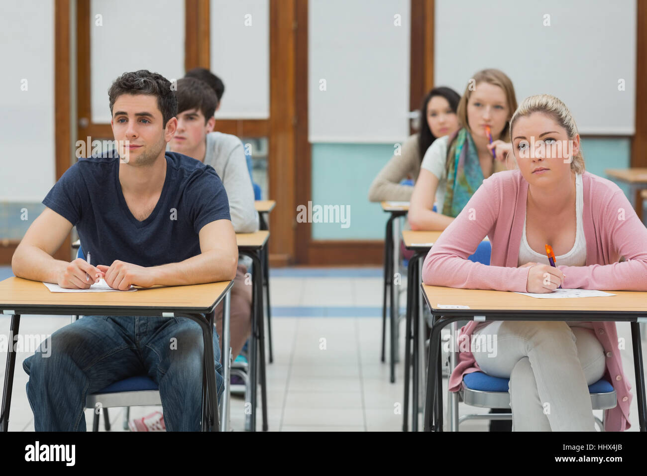 Students sitting at desk looking up in exam hall in college Stock Photo