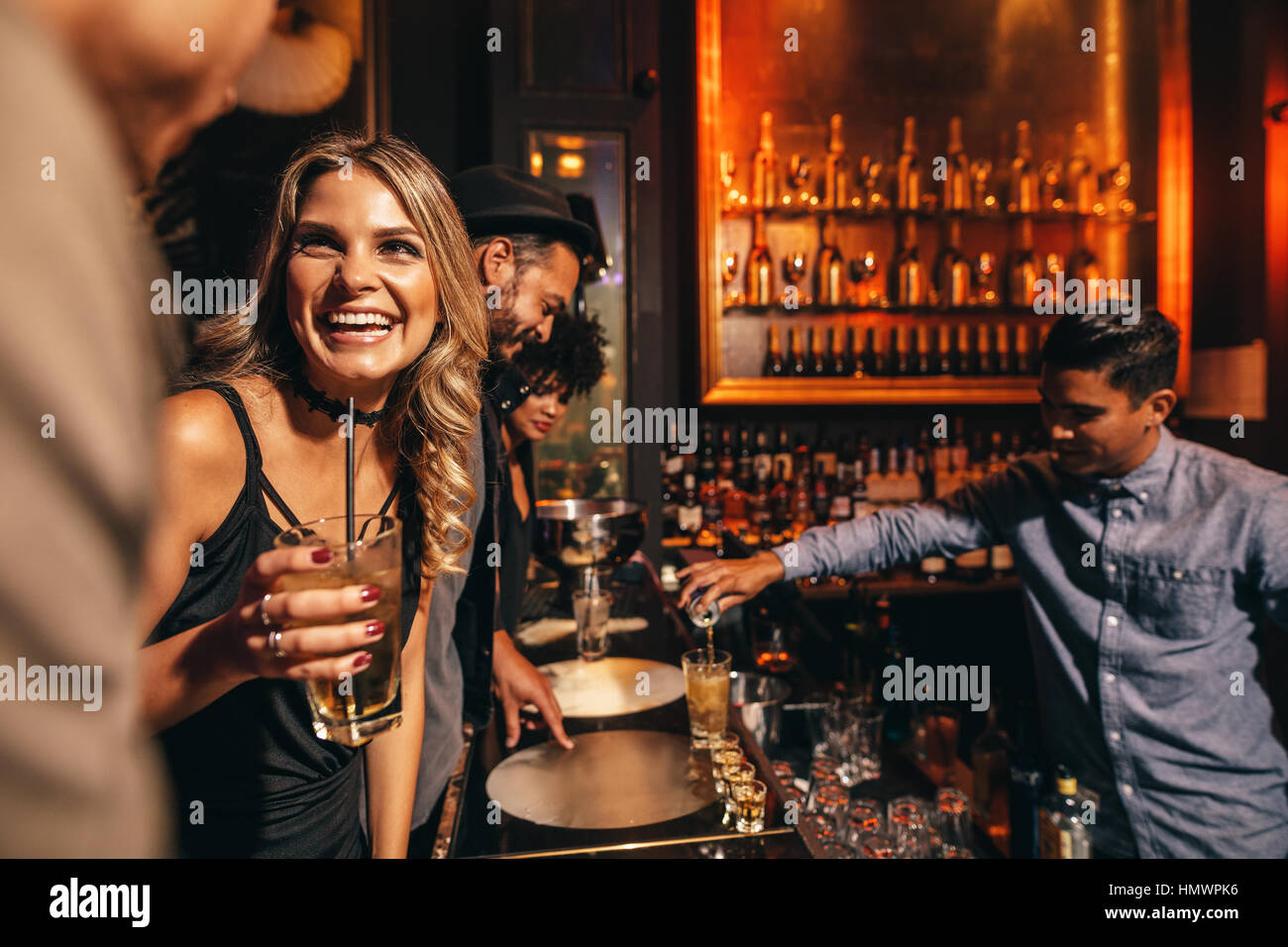 Beautiful young woman with her friends at bar. Young people enjoying a night at club. Stock Photo