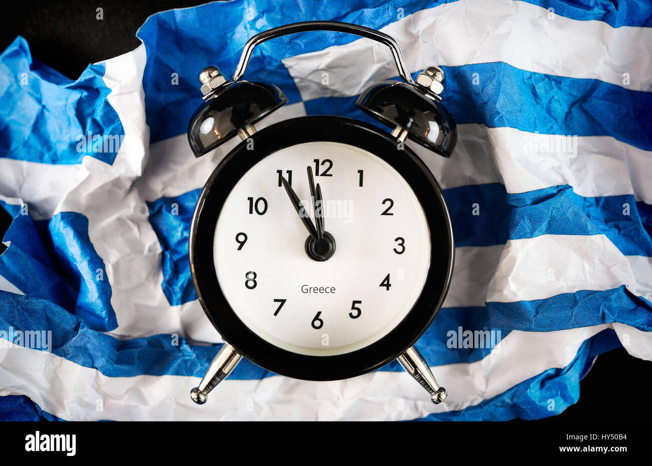 Alarm clock on five before twelve on crumpled up Greece flag, symbolic photo debt quarrel, Wecker auf Fuenf vor Zwoelf auf zerknuellter Griechenlandfa Stock Photo