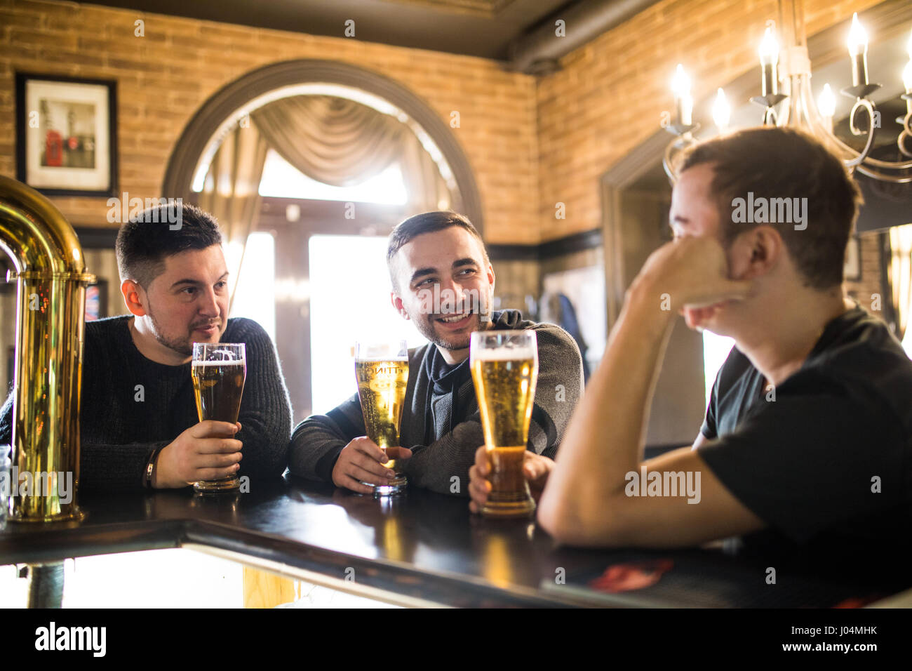 Cheerful old friends having fun and drinking draft beer at bar counter in pub. Stock Photo