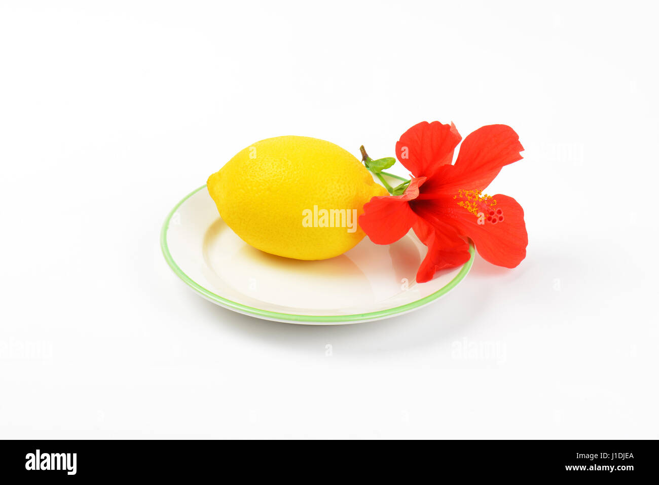 ripe lemon with red hibiscus bloom on white plate Stock Photo