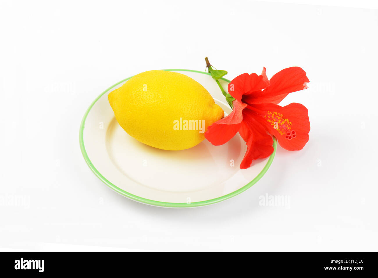 ripe lemon with red hibiscus bloom on white plate Stock Photo