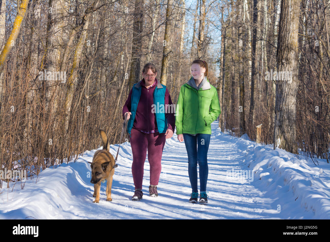 A mother and daughter walking their dog on a sunny winter day. Stock Photo