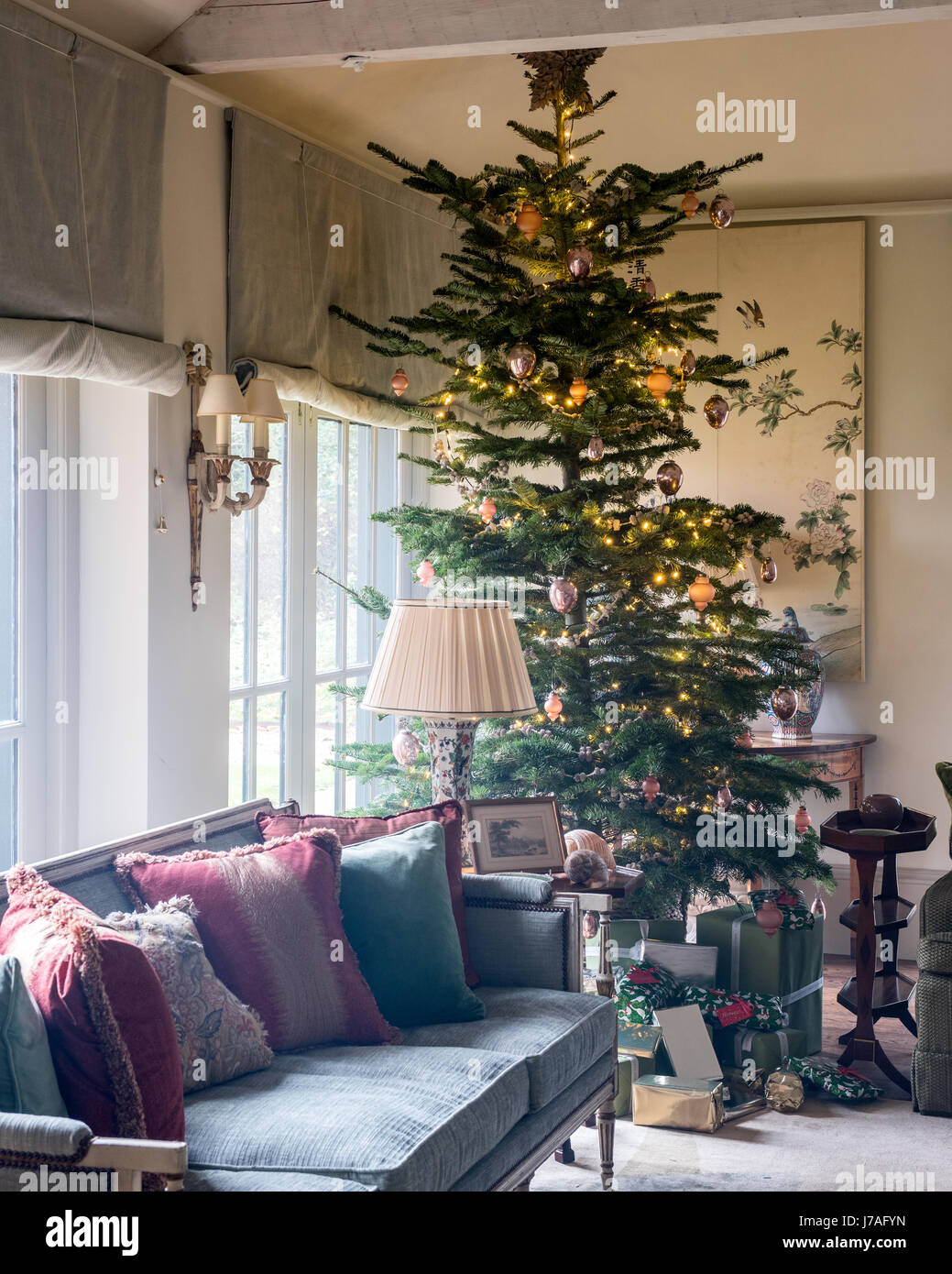 Tall christmas tree in corner of spacious sitting room with settee and old chinese painted panels. The sofa upholstery and blinds are from Colefax and Stock Photo