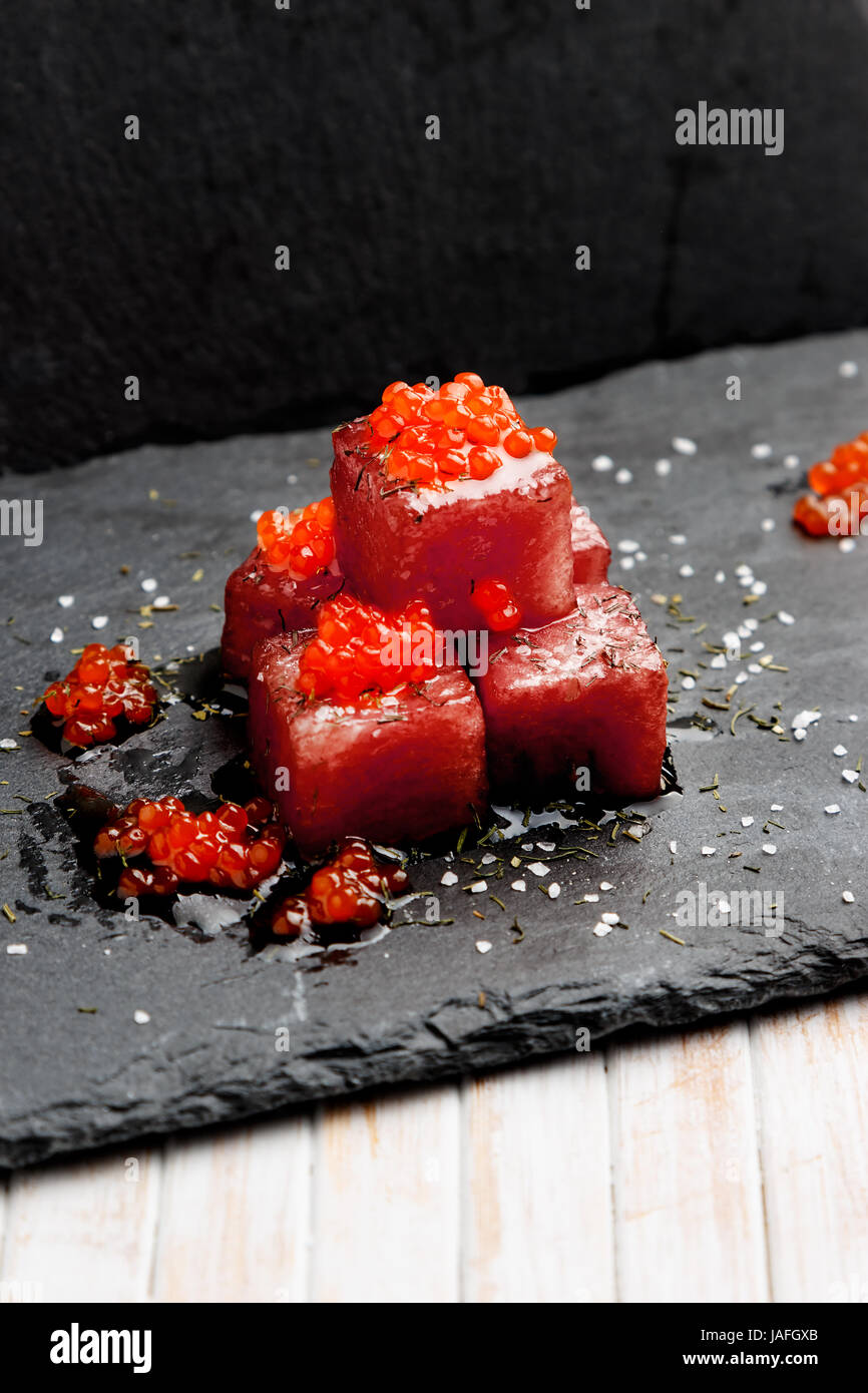 Tuna sashimi dipped in soy sauce with salmon roe, thick salt and dill on slate stone. Raw fish in traditional Japanese style. Vertical image. Stock Photo