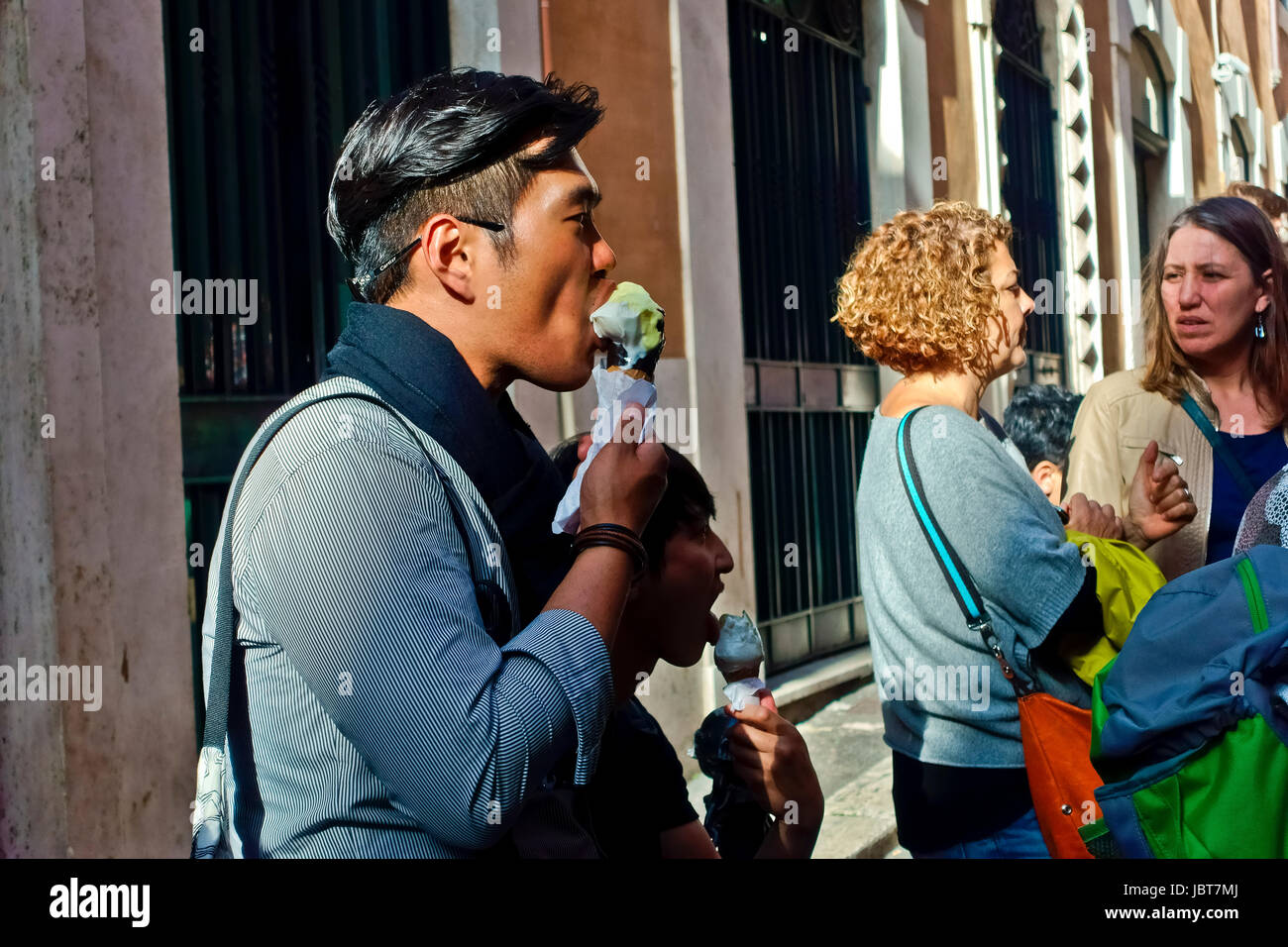 Young asian man enjoying eating ice cream cone outdoors in a roman alley Rome, Italy, Europe, European Union, EU. Stock Photo