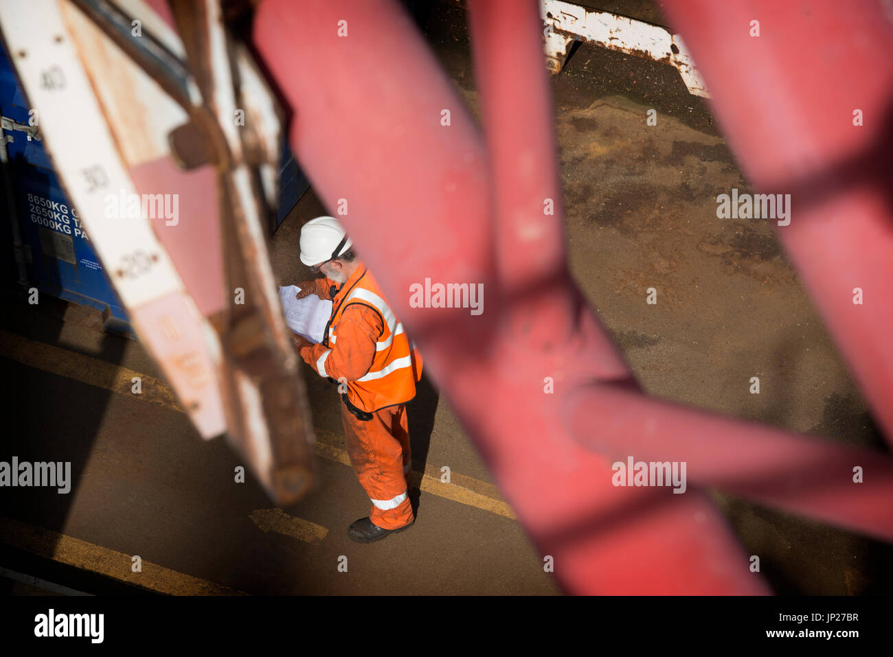 Offshore materials coordinator (store man) reading the manifest whilst wearing orange coveralls / overalls. credit: LEE RAMSDEN / ALAMY Stock Photo