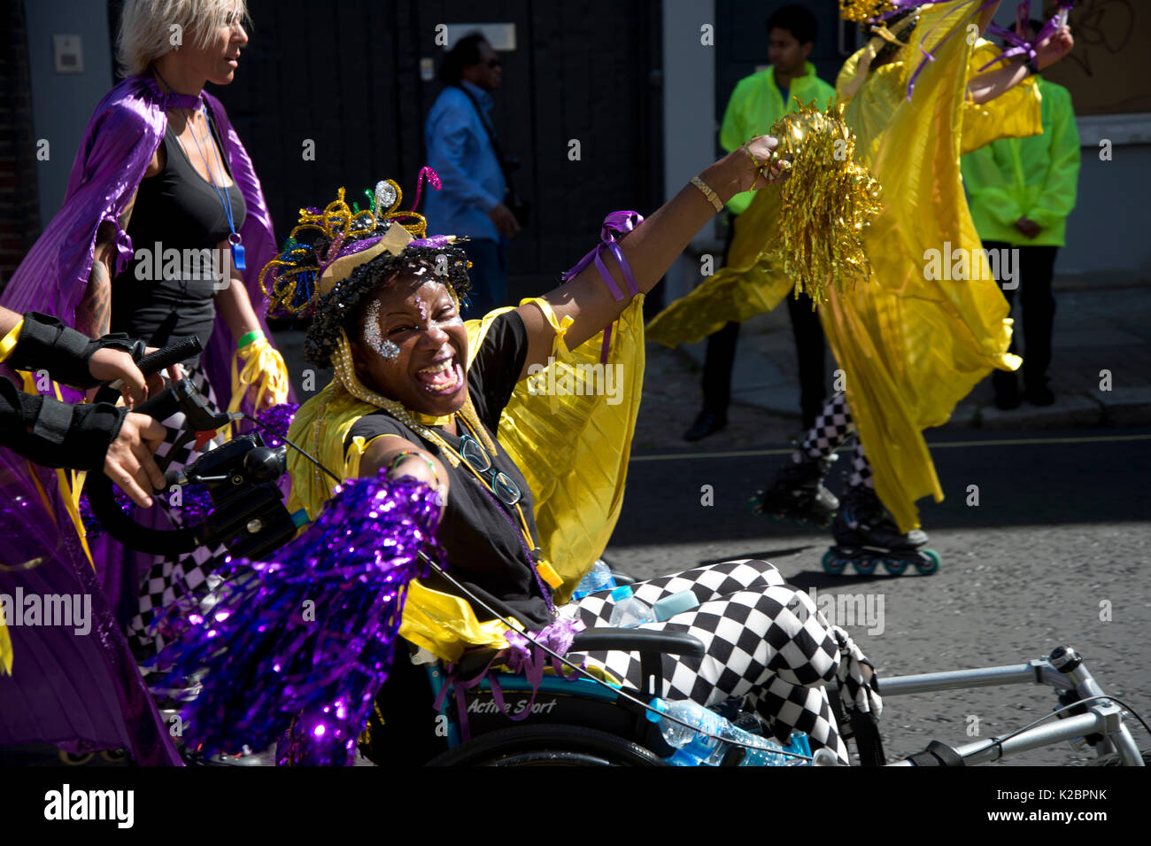 Notting Hill Carnival August  2017. A carnival reveller dances in her wheelchair, alongside a group of roller bladers. Stock Photo