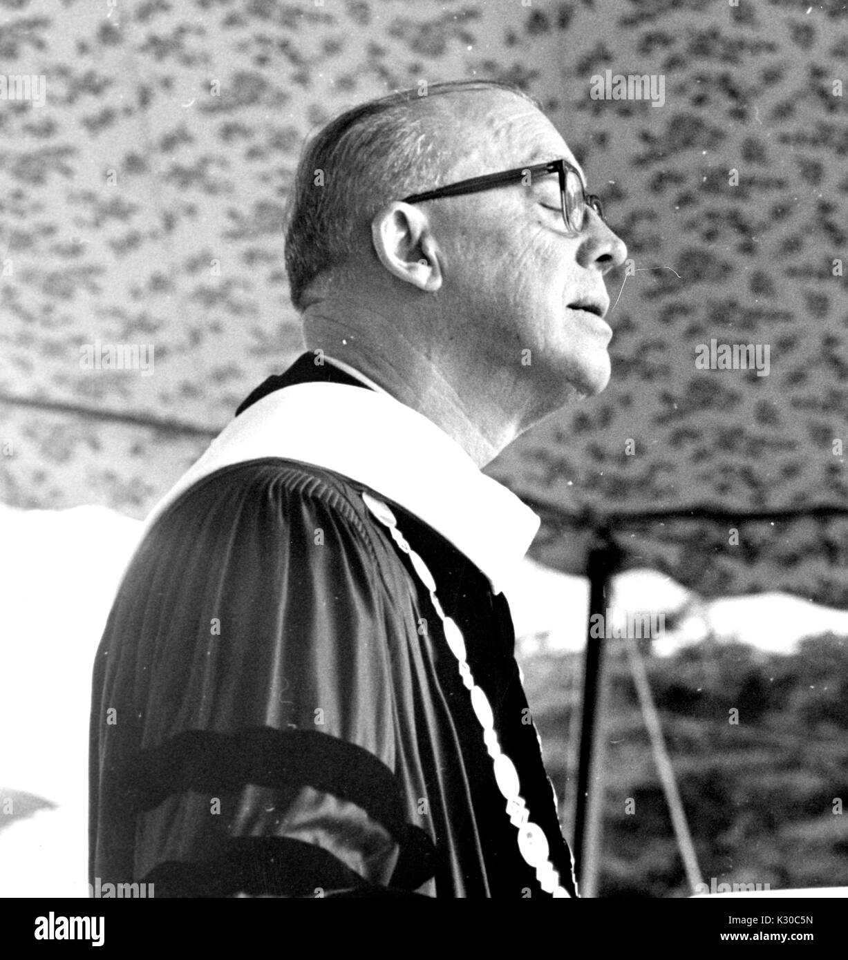 On Commencement Day, President of Johns Hopkins University Milton Stover Eisenhower wears graduation garb to address the crowd from a podium, his profile visible and his eyes closed, Baltimore, Maryland, June 13, 1967. Stock Photo