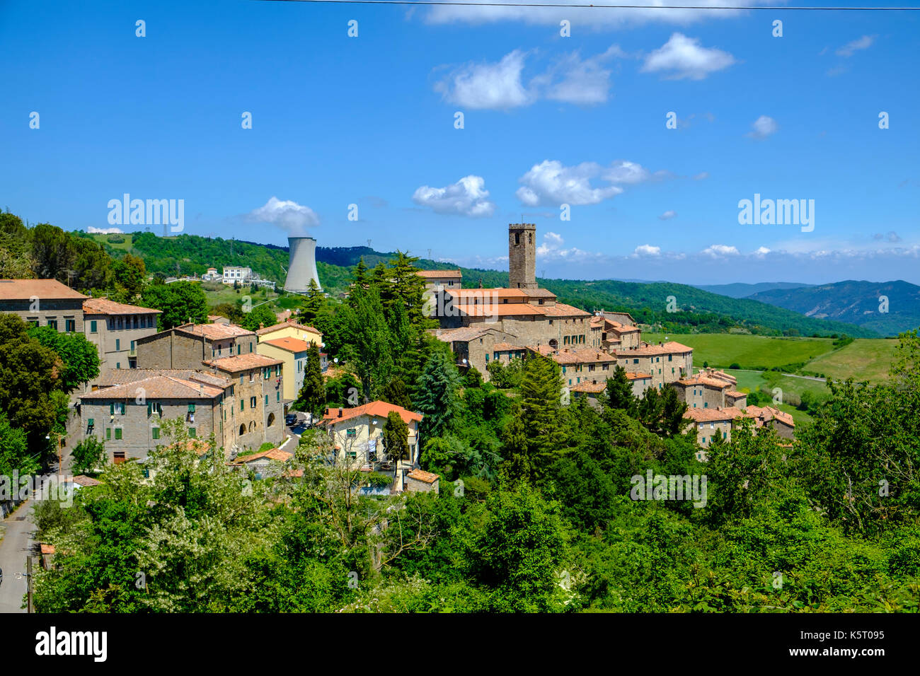 The stone houses of the small village are located at the slope of a hill, surrounded by trees and a geothermal power plant Stock Photo