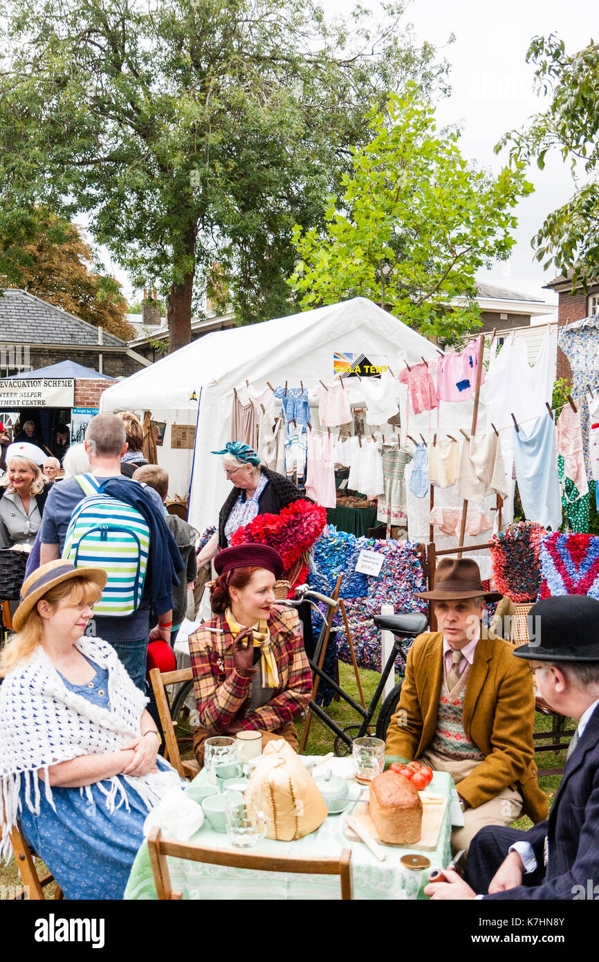 Two mature couples dressed in upper class clothing circa 1940's re-enacting a world war two picnic at a table with washing hanging behind them. Salute to the 40's weekend at Chatham Historic Dockyard. Elderly man smoking a pipe. Stock Photo