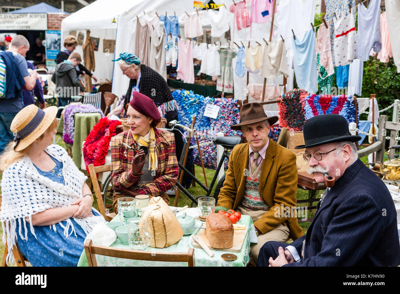 Two mature couples dressed in upper class clothing circa 1940's re-enacting a world war two picnic at a table with washing hanging behind them. Salute to the 40's weekend at Chatham Historic Dockyard. Elderly man smoking a pipe. Stock Photo