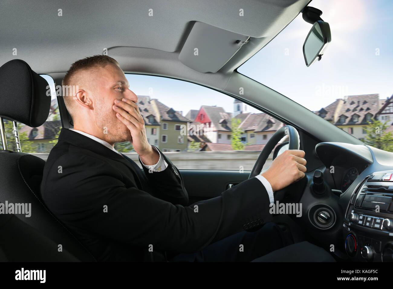 Portrait Of A Young Businessman Yawning While Driving Car Stock Photo