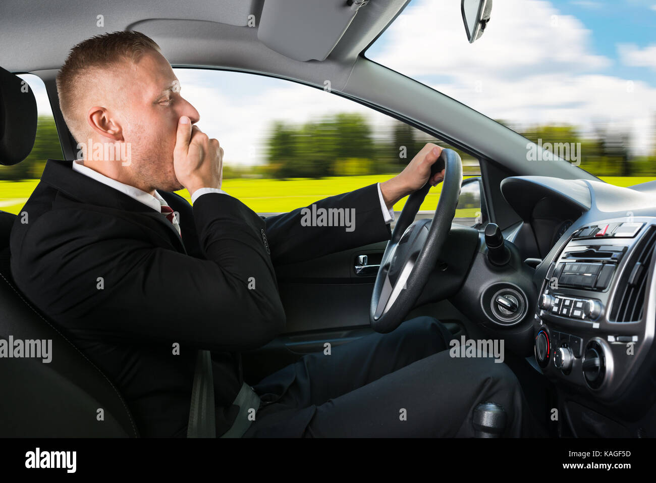 Portrait Of A Young Businessman Yawning While Driving Car Stock Photo