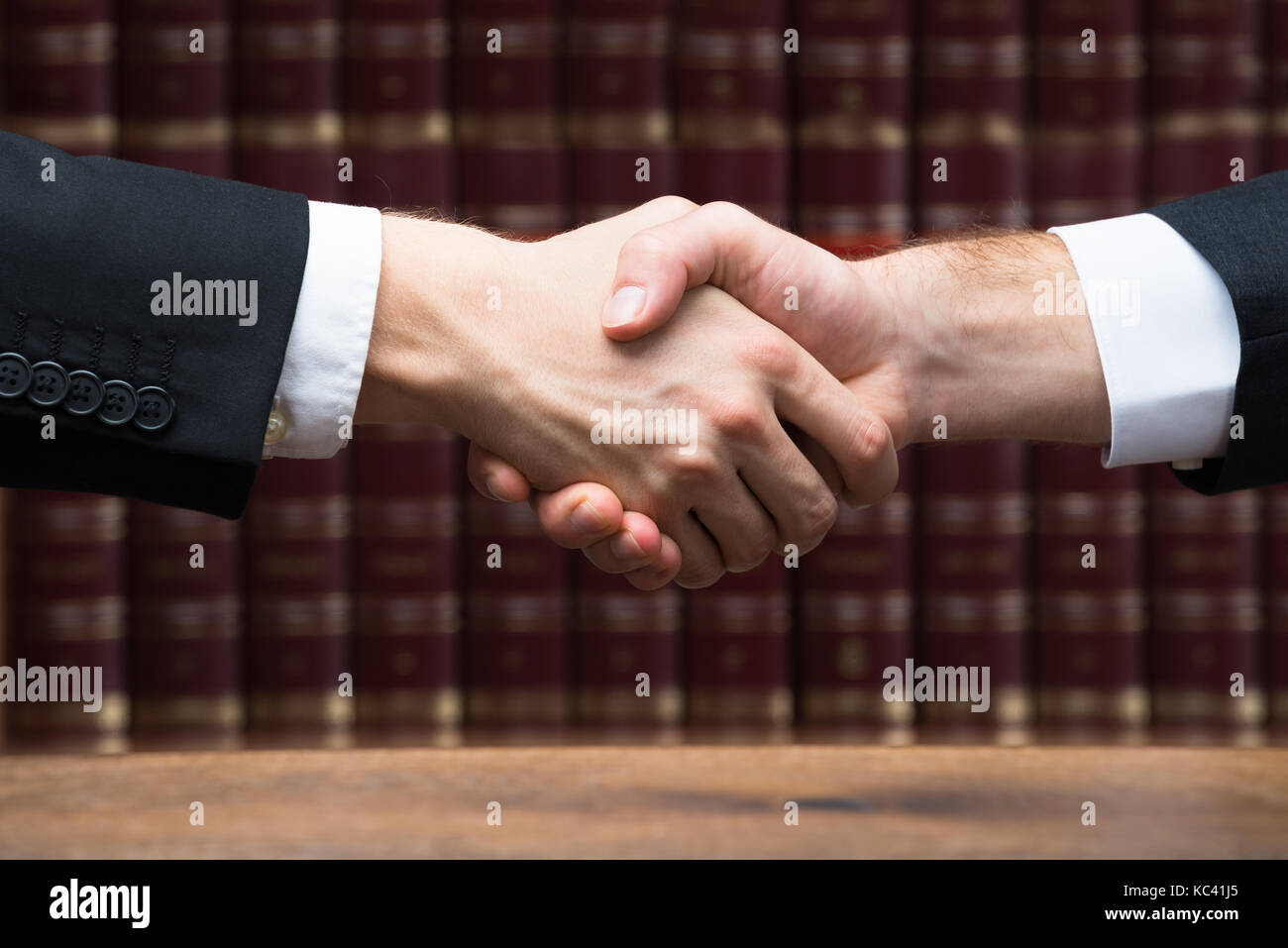 Cropped image of judge and client shaking hands against books at courtroom Stock Photo