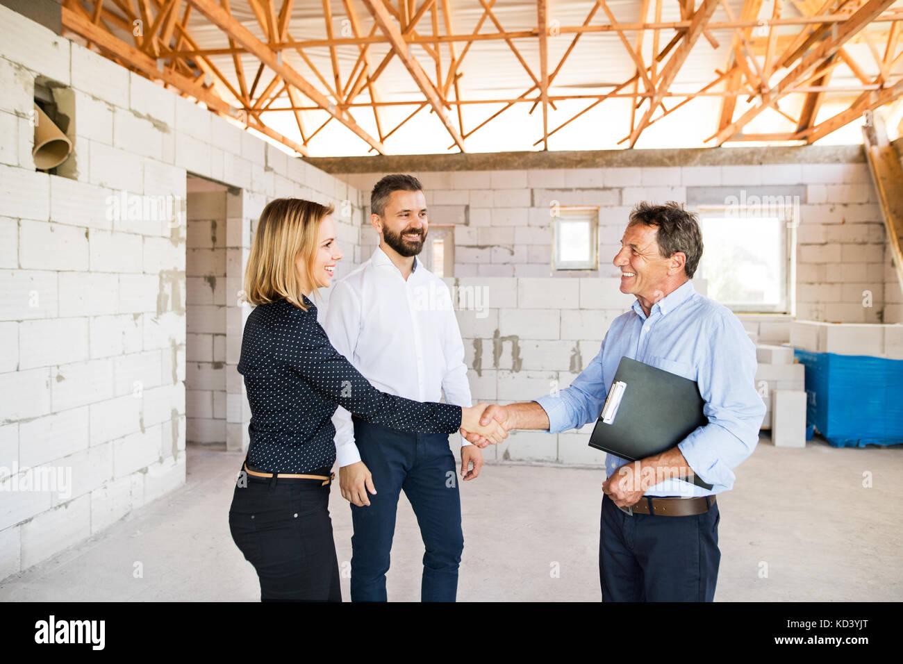 Young couple with architect or civil engineer looking at plans of their new house, discussing issues at the construction site. Stock Photo