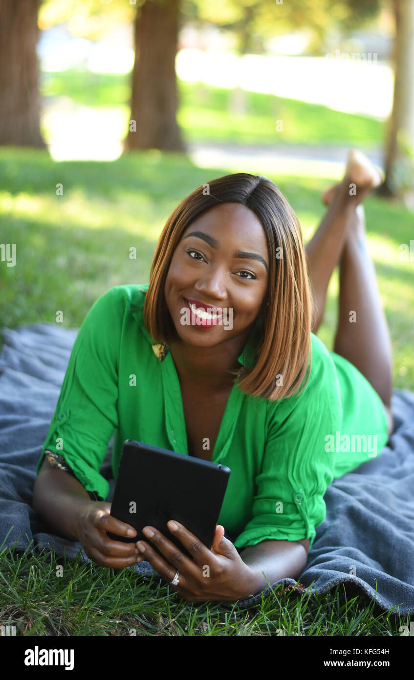 A young black women laying on a blanket using her tablet in a park Stock Photo