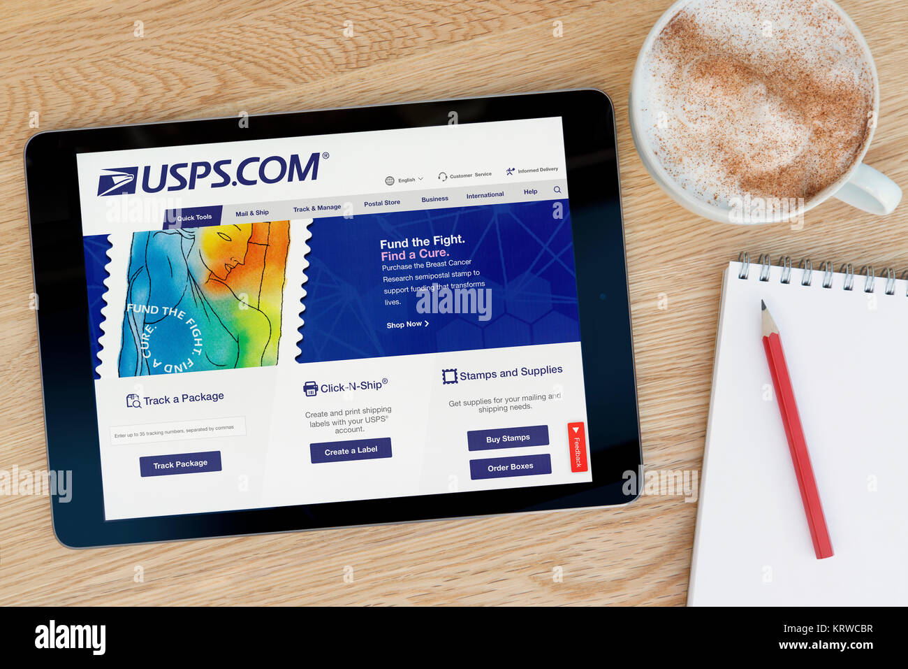 The USPS website on an iPad tablet device which rests on a wooden table beside a notepad and pencil and a cup of coffee (Editorial only) Stock Photo