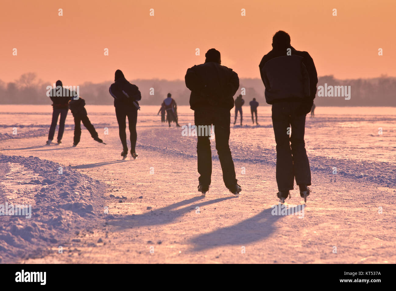 Ice Skaters on frozen lake seen on their back under orange sunset Stock Photo