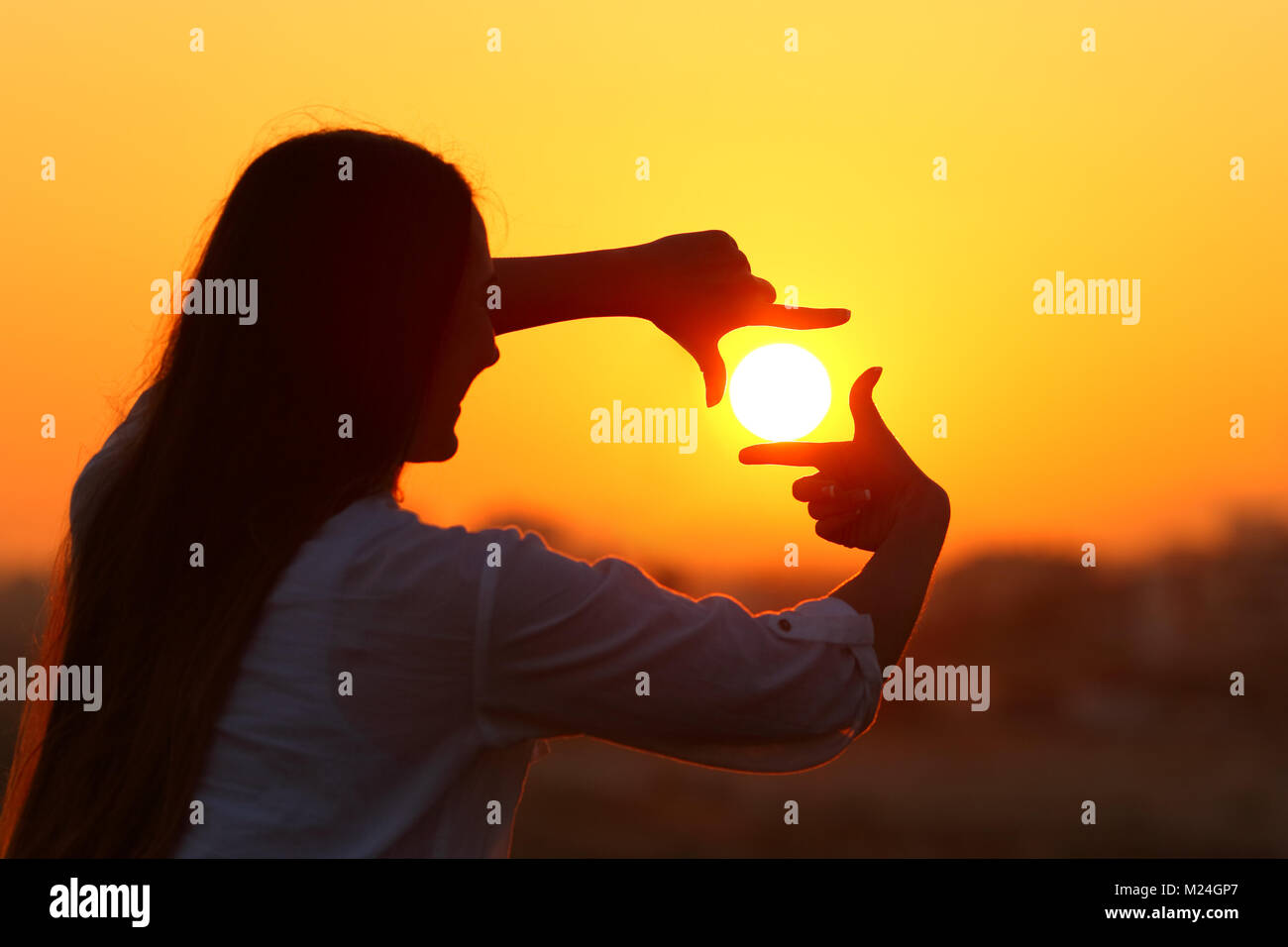 Backlight portrait of a woman silhouette framing sun with fingers at sunset Stock Photo