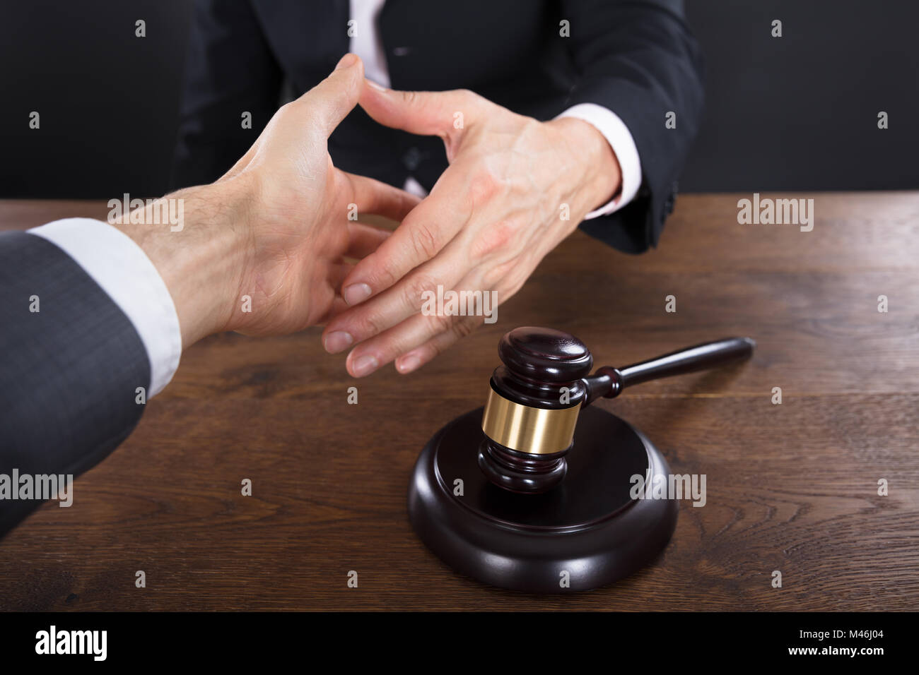 Client And Judge Shaking Hands With Each Other Near Gavel On Wooden Desk Stock Photo