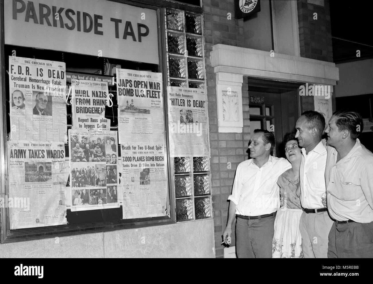 A group gathers to read newspaper headlines outside a Chicago tavern at the end of World War II, ca. 1945. Stock Photo