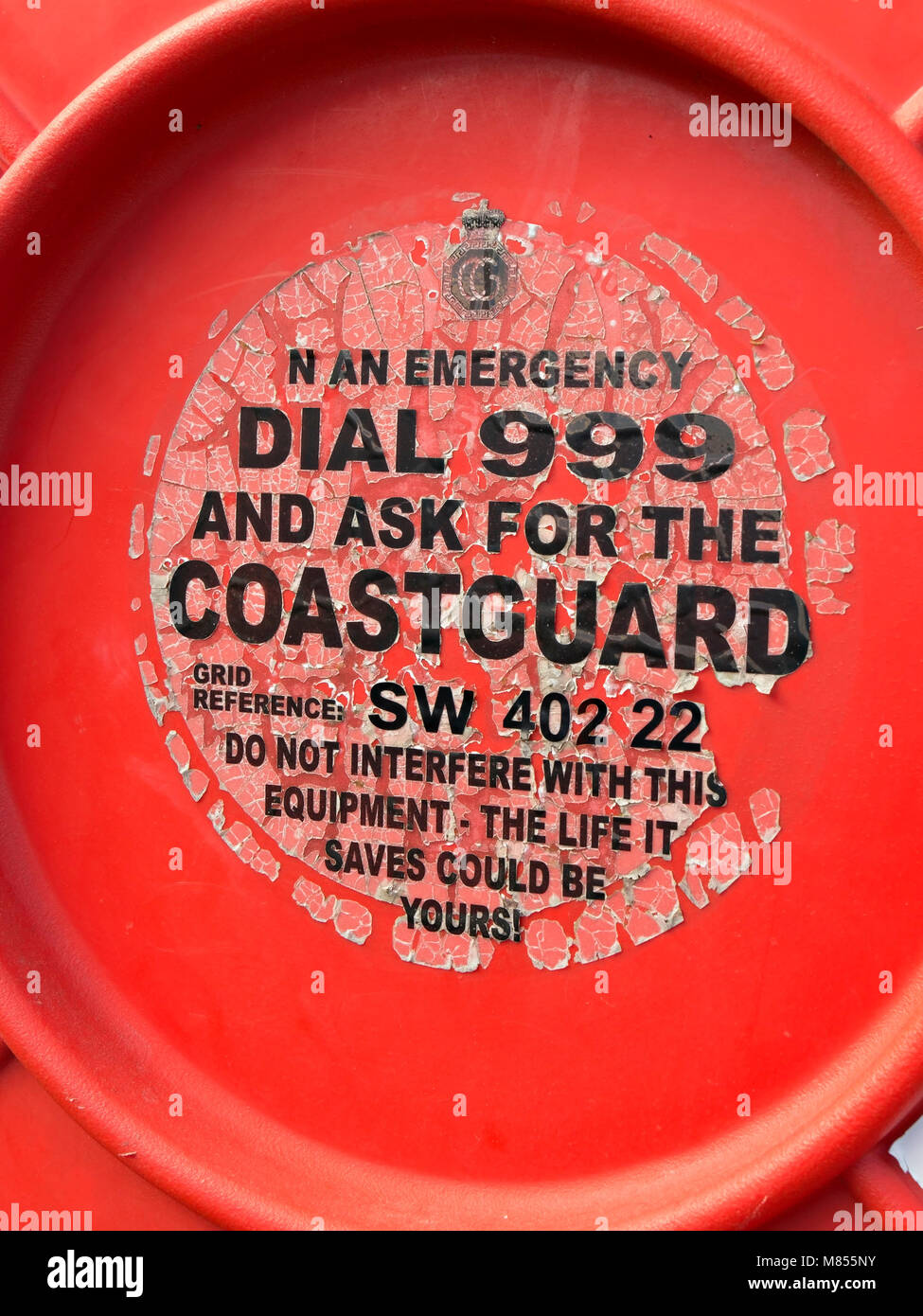 Old faded and peeling emergency services label on lifebuoy housing, Penberth Cove Harbour, Cornwall, England, UK Stock Photo