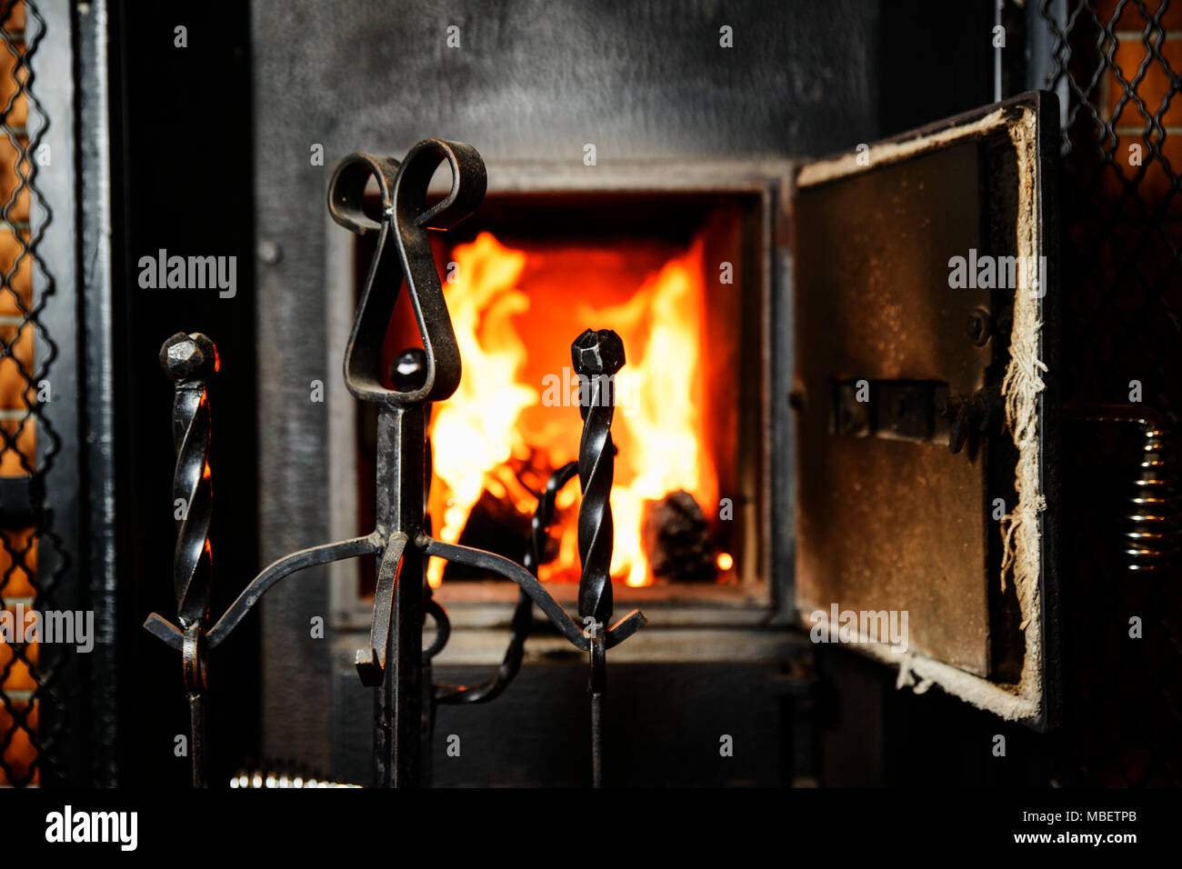 Accessories for care of the stove in front of an open firebox with a red yellow flame Stock Photo