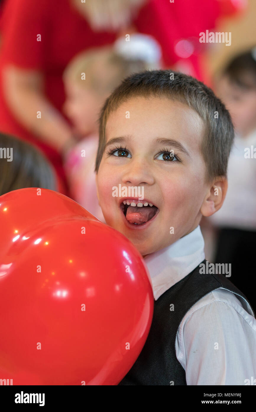 little funny boy with red balloon. portrait of a funny kid holding a big red balloon against an abstract background. Stock Photo