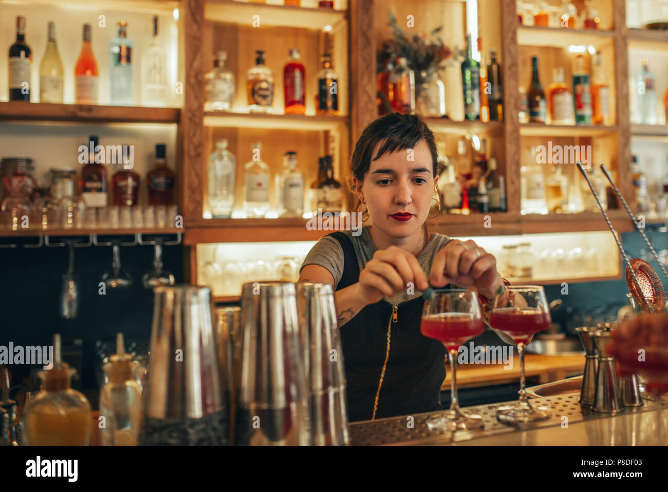 Young female bartender standing behind a bar counter making cocktails  Stock Photo