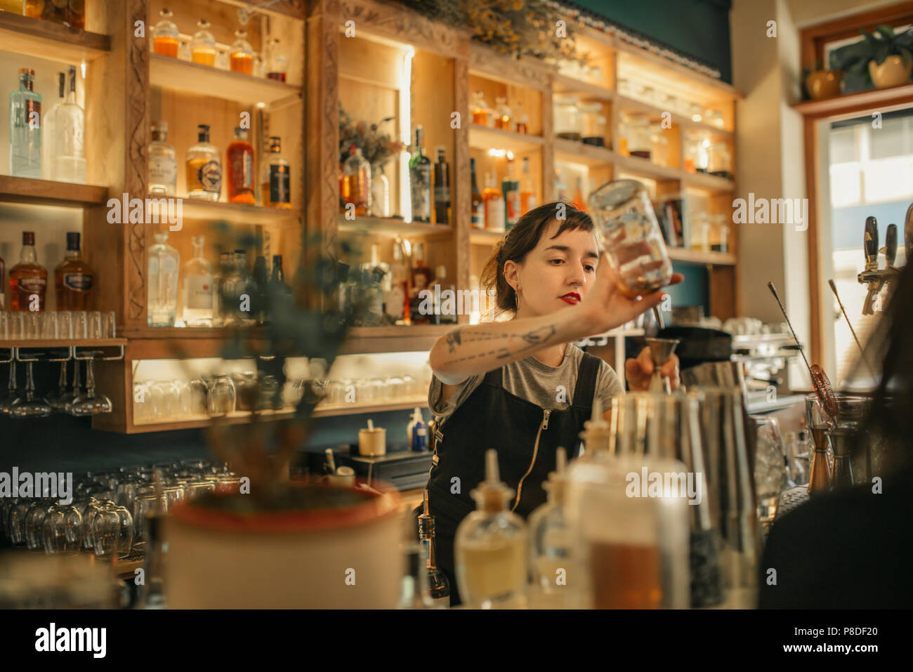 Young female bartender pouring cocktails behind a bar counter Stock Photo