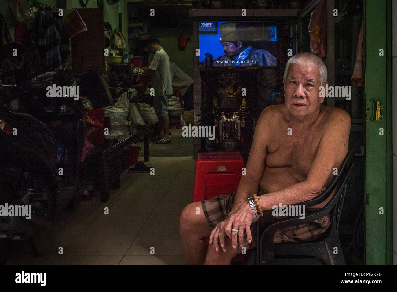 An elderly man sits outside of his shop in Ho Chi Minh City, Vietnam Stock Photo