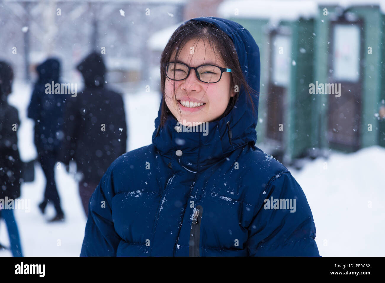 Happy young Asian female teenager in thick blue winter jacket enjoy being outside during winter snow, good for happy lifestyle or positive attitude co Stock Photo